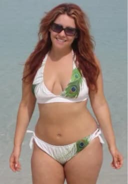 Woman with long reddish-brown hair in a white bikini with green accents, standing on a beach.