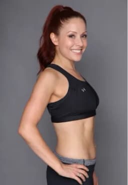 Smiling woman with red hair in a ponytail wearing a black sports bra and exercise pants.